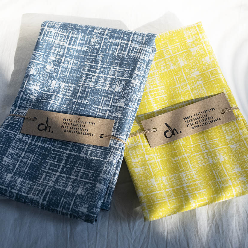 Routa-keittiöpyyhkeet, värivaihtoehdot sininen ja keltainen, taiteltuina limittäin, päällekkäin, valkoista taustaa vasten.