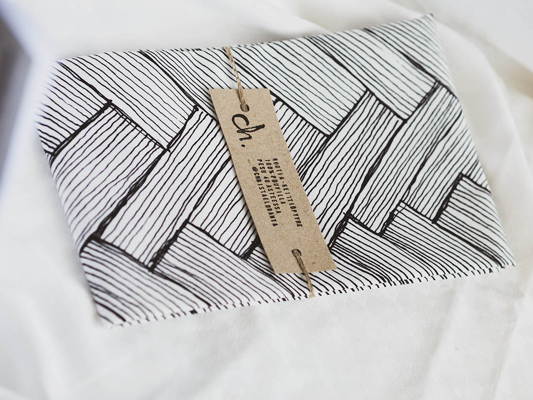 Mustavalkoinen keittiöpyyhe Ruotia-kuosilla taiteltuna ja vyötteen kanssa