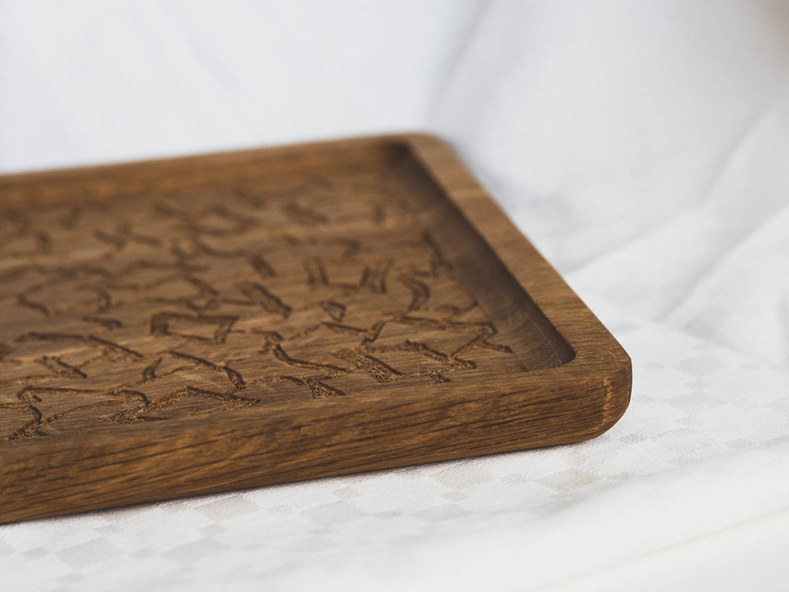 Saippuakukka-tarjoilulautanen valkoista taustaa vasten. Materiaali on tammea. Tarjoilulauta on neliön muotoinen, siinä on pienet reunat ja jyrsitty kukkakuvio keskellä.